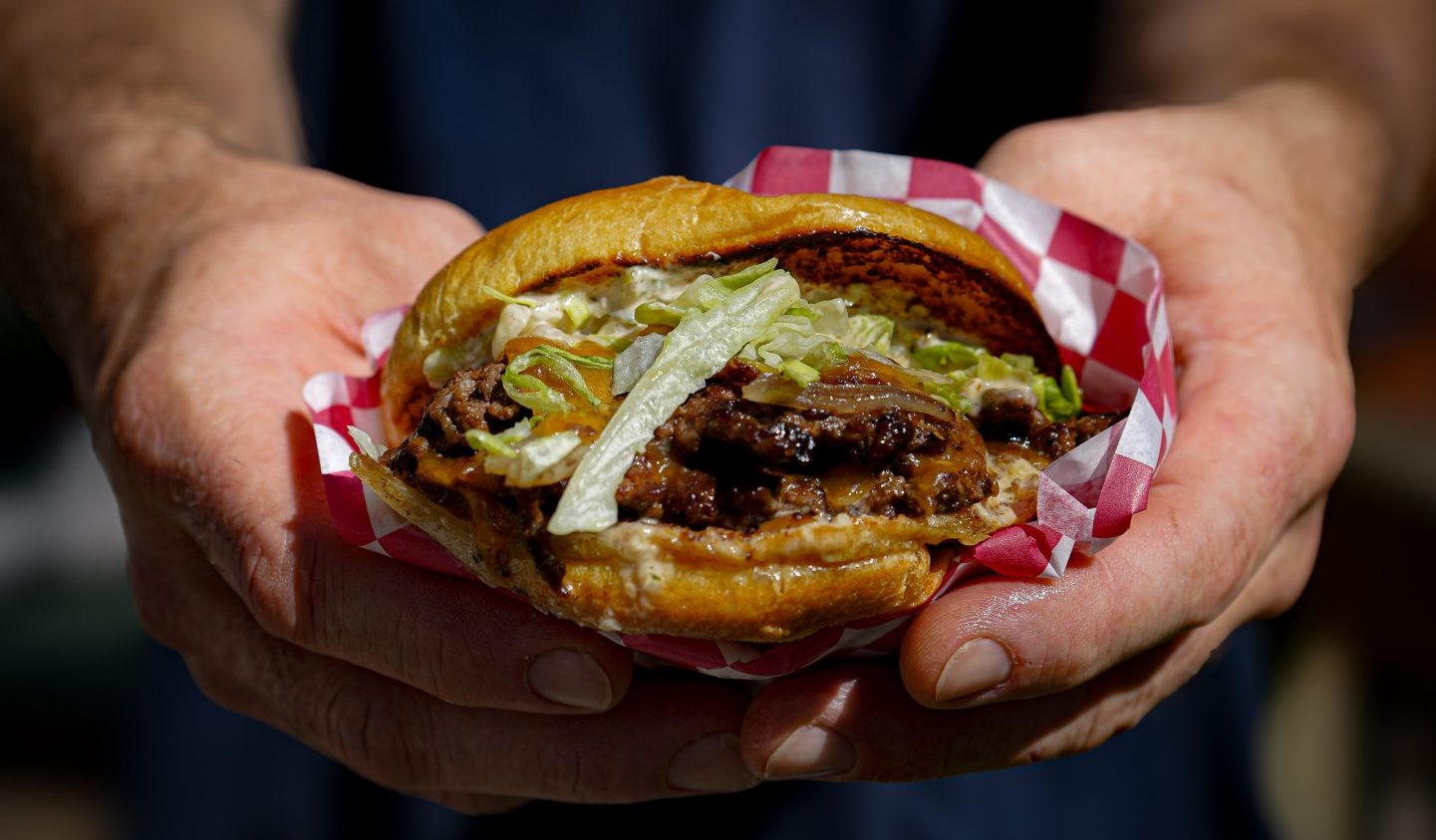 Chef Sean's Hands Presenting a Delicious Burger